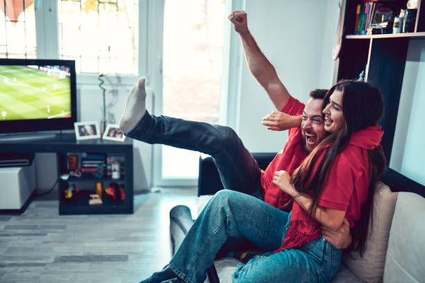 Couple Laughing And Cheering During Sports Match On TV